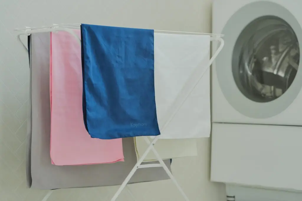 Kajimoreのバスタオルが色違いで物干しスタンドに干されている画像。洗濯機のドラムが背景に写っています。
