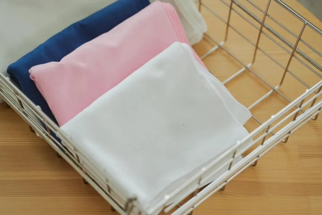 Kajimoreのタオル3色（ブルー、ピンク、ホワイト）が、ワイヤーバスケットに重ねて収納されている画像。