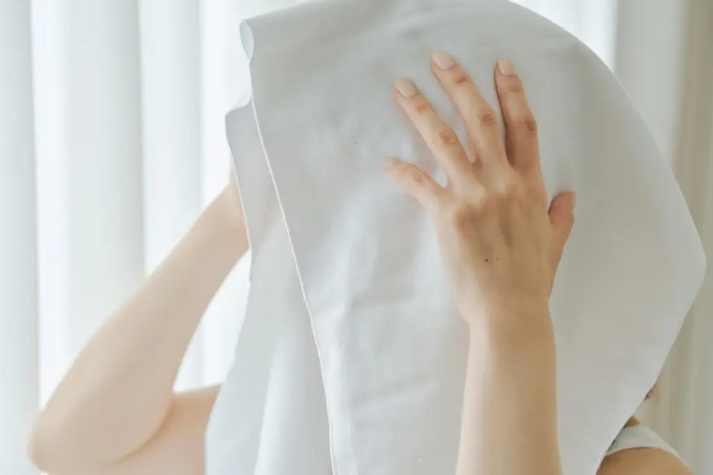 Kajimoreのホワイトのタオルで顔を拭く女性の手元のクローズアップ画像。タオルの質感がよく見えます。