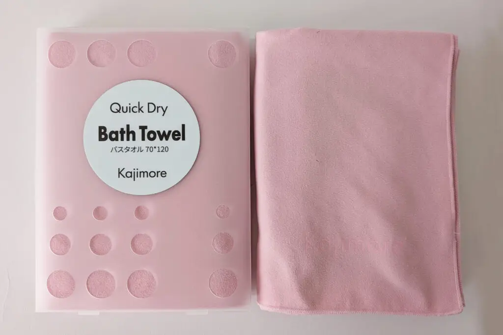 ピンクのバスタオルとハードケースのセット。タオル表面にはさりげなく「Kajimore」のロゴが同系色で刻印されている。