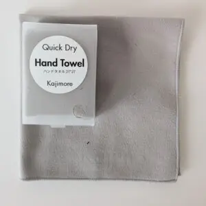 ライトグレーの速乾ハンドタオルとハードケース。 洗練されたモノトーンの色味が半透明のスリーブケース越しに確認できる。