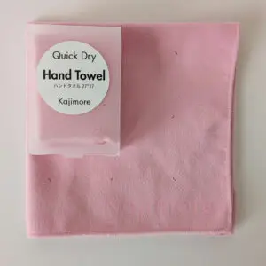 ピンクの速乾ハンドタオルとハードケースのセット。 落ち着いた大人なピンクの色味が特徴で、タオルのロゴ刻印も見える。