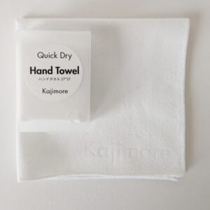 ホワイトの速乾ハンドタオルと、専用ハードケースのセット。 タオル中央部には「Kajimore」のブランドロゴがさりげなく刻印されている。